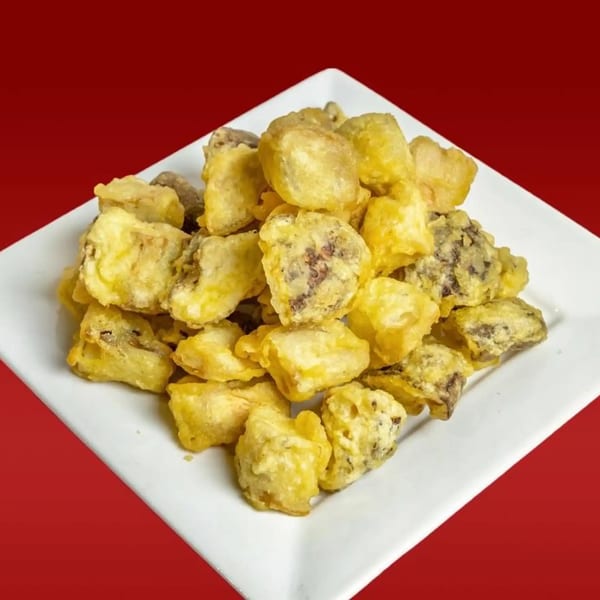 A white square plate filled with golden-brown Taiwanese fried mushrooms against a red background.