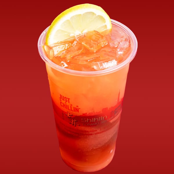 A Shihlin Taiwan Street Snacks drink, orange with ice and a lemon slice, against a red background.
