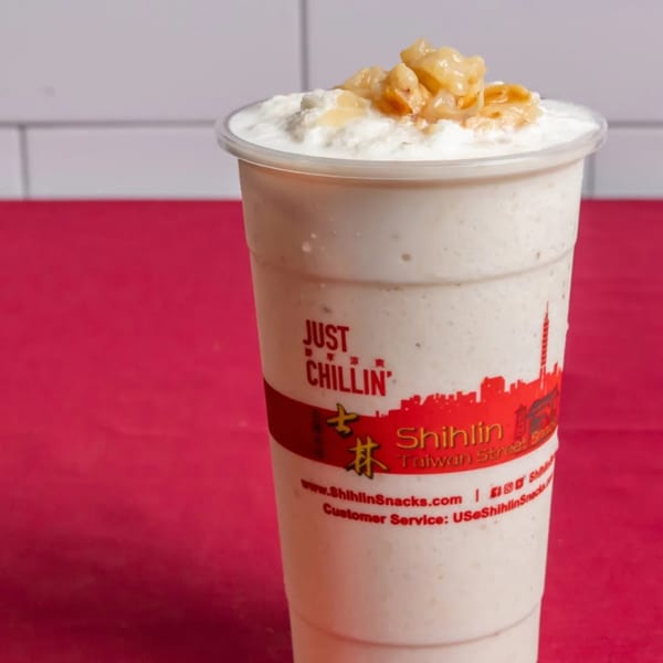 A Shihlin Taiwan Street Snacks drink with a creamy top and golden toppings on a red surface.
