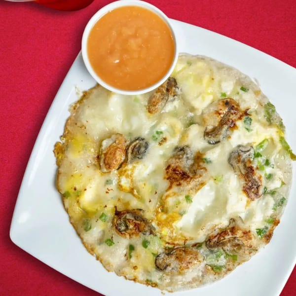 Taiwanese oyster omelet with green onions and a side of orange sauce on a white plate.
