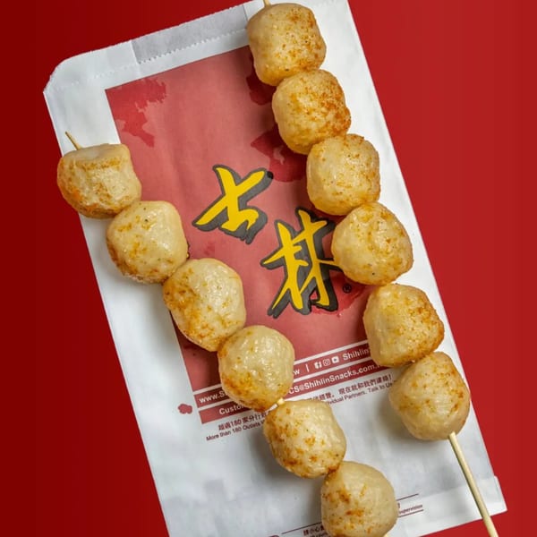 Taiwanese fishball skewers with seasoning, resting on a Shihlin Taiwan Street Snacks paper bag.