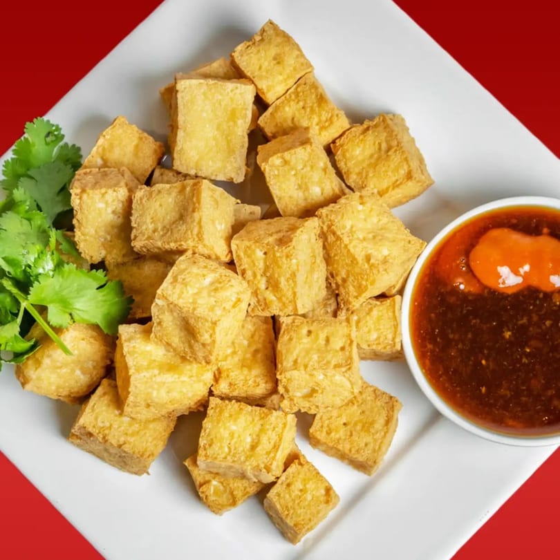 Crispy golden fried tofu cubes with fresh cilantro and a side of spicy dipping sauce.