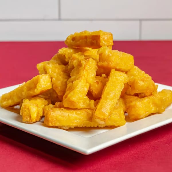 A white plate piled high with golden-brown Taiwanese fried sweet potato fries on a red surface.